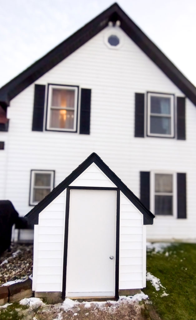 White shed with a white house behind it